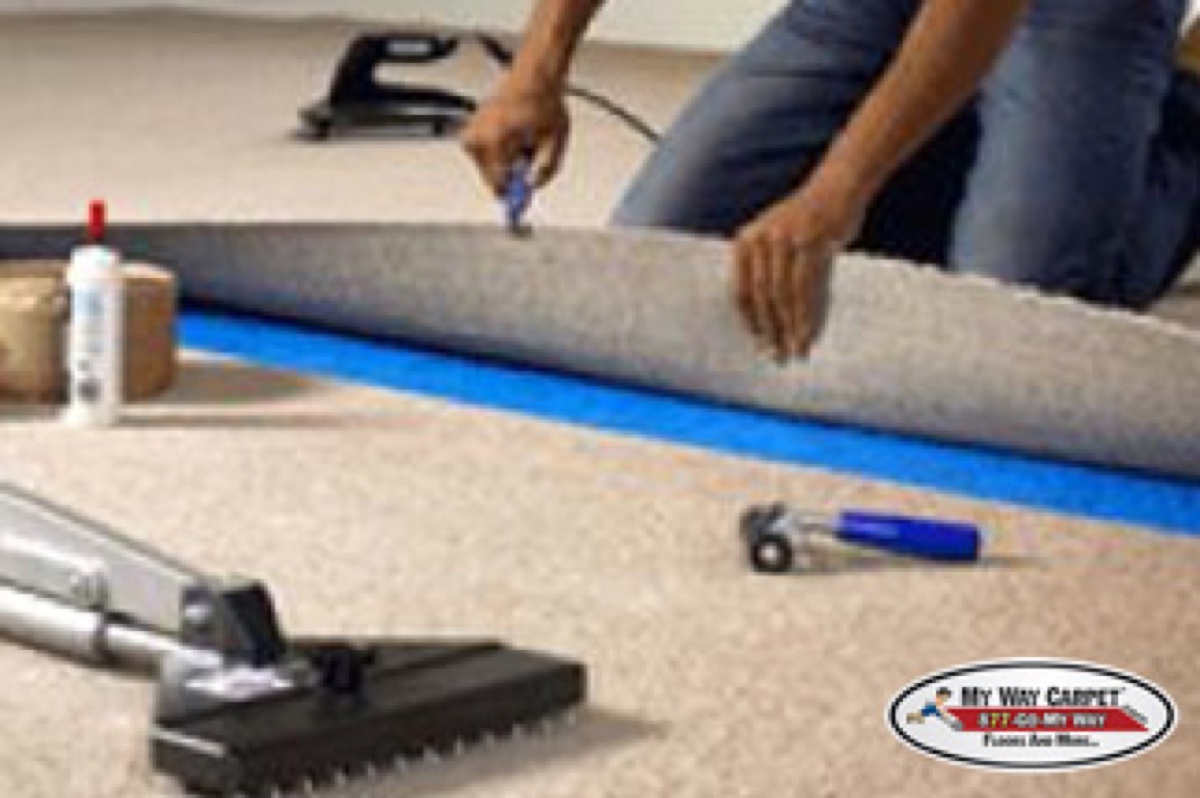 Installer applying blue seam tape adhesive under a carpet seam